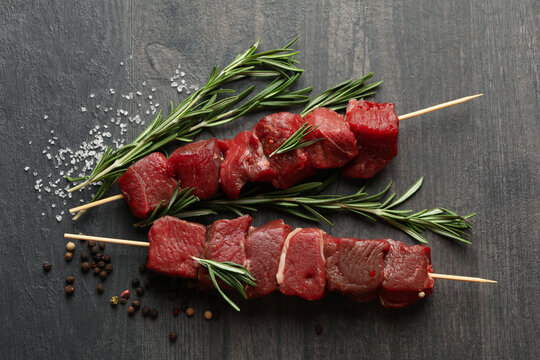 Skewers with raw meat and spices on dark background