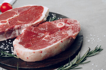 Raw rib-eye beef steak on wooden cutting board on gray background