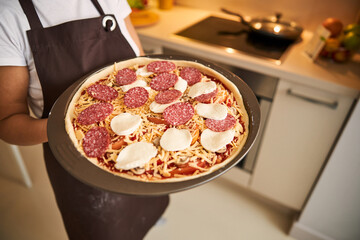 Raw pizza on the baking pan in hands of woman