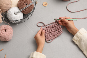 Woman crocheting with threads at grey table, closeup. Engaging hobby