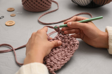 Woman crocheting with threads at grey table, closeup. Engaging hobby