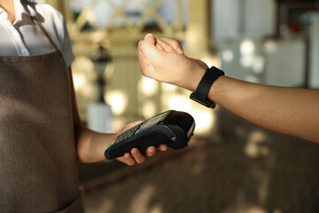 Man using terminal for contactless payment with smart watch in cafe, closeup