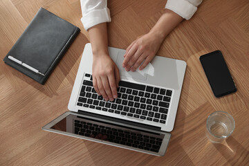 Young woman using laptop for search at wooden table, top view