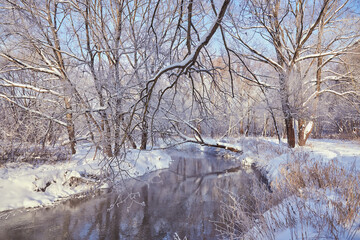 A small river flows between snow-covered trees on a clear winter day.