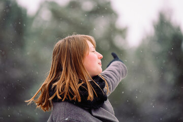 A profile photo of a girl who points her index finger into the distance, looking away. Winter forest background. Enlarged photo.