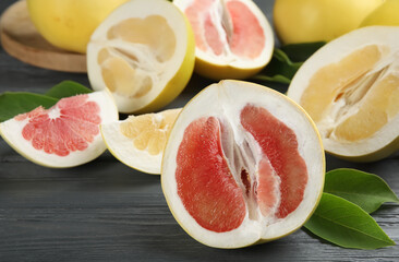 Fresh cut pomelo fruits with leaves on grey wooden table, closeup