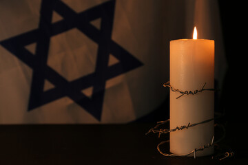 Barbed wire and burning candle on black background. Holocaust memory day