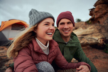 Happy young couple relaxing during camping sitting outside tent looking away during winter