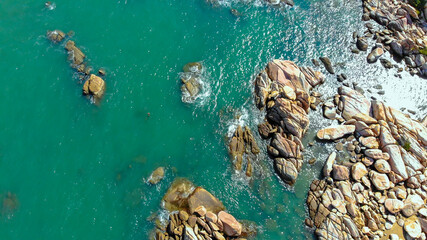 Aerial drone top view of ocean's beautiful waves crashing on the rocky island coast at Ke Ga beach in Mui Ne, Phan Thiet, Binh Thuan, Vietnam