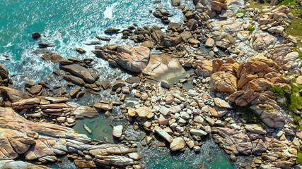 Aerial drone top view of ocean's beautiful waves crashing on the rocky island coast at Ke Ga beach in Mui Ne, Phan Thiet, Binh Thuan, Vietnam