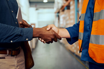 Midsection view of two male workers shaking hands at factory - obrazy, fototapety, plakaty