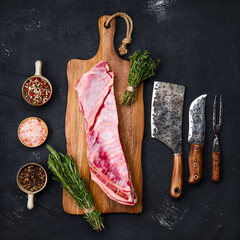 Raw lamb breast and flap on wooden cutting board with herbs and seasoning