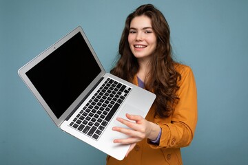 Photo of Beautiful smiling happy young woman holding computer laptop looking at camera having fun wearing casual smart clothes isolated over wall background