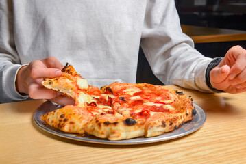 Young man eating a slice of pizza margherita. Still life, eating out concept. At restaurant or at home, pizza delivery.