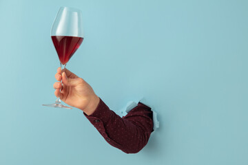 Male hand holding wine glass and breaking through blue paper background.