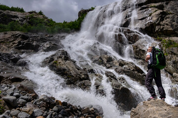 Obraz premium Man hiking with backpack looking at waterfall. Portrait of male adult back standing outdoor.