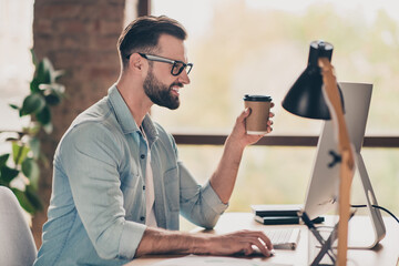 Photo portrait of guy holding coffee cup in hand working on pc at table in modern industrial office indoors