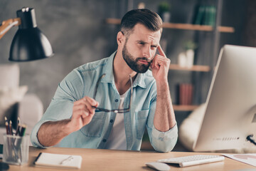 Photo portrait of tired man touching temple with finger having headache at table in modern industrial office indoors