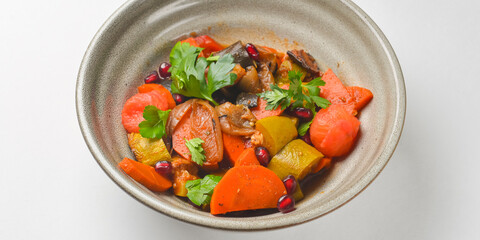 Baked vegetable salad in a cermaic bowl over white background. Delicious healthy autumn or winter salad.