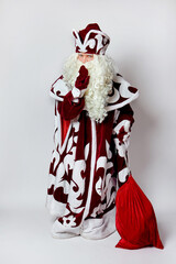 Obraz premium Russian Santa Claus shows a gesture of silence, a gloved finger near his lips. With a big red bag of gifts. On a white background.