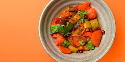 Baked vegetable salad in a cermaic bowl over orange background. Delicious healthy autumn or winter salad.