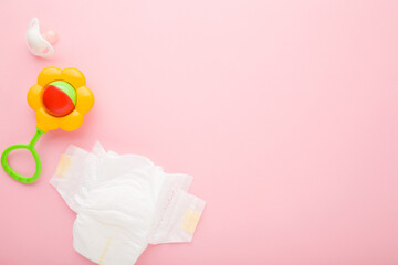 White baby diaper, soother and colorful flower rattle toy on light pink table background. Pastel color. Closeup. Empty place for text. Top down view.