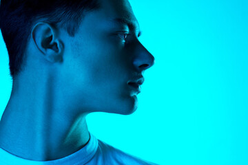 At side. Handsome caucasian man's portrait isolated on blue studio background in neon, monochrome. Beautiful male model. Concept of human emotions, facial expression, sales, ad, fashion and beauty.
