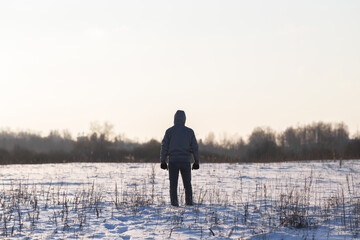 One young adult man standing alone on white snowy field and looking far away. Cold winter day. Back view. Empty place for text, quote or sayings on light sky background. - Powered by Adobe