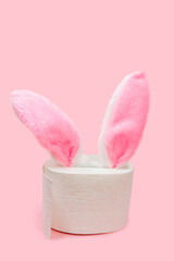 pink Rabbit ears peek from toilet paper on pink background. Bunny ears out of toilet paper roll. Easter holiday 2021 during Covid-19. coronavirus Quarantine Pandemic concept. vertical image