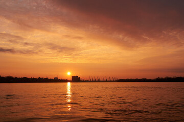 Silhouettes of port cranes and the setting sun in a river port on a winter evening