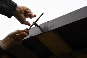 The roofer is installing a new sheet metal roof. Roofing tools, roof screw installation. An example...