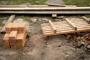 On the ground is a pile of new bricks, pine boards. Preparing material for the rack