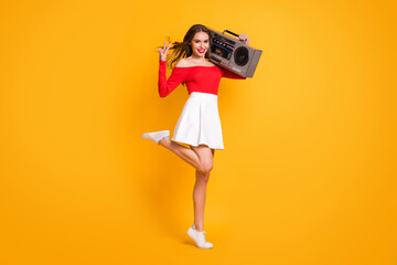 Full length body size photo smiling girl keeping boom-box showing v-sign gesture isolated on vibrant yellow color background