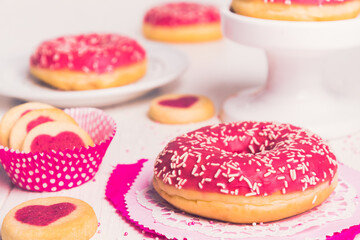 Obraz na płótnie Canvas Pink glazed donut on white, decorated with cookies and further donuts in the background