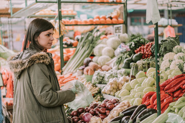 Beautiful female in market choosing vegetables. Healthy living and eating. Market vegetables prices going up 