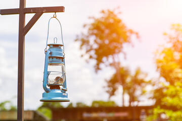 Old blue hurricane lamp hanging on wooden pole with sunlight. Oil kerosene lamp.