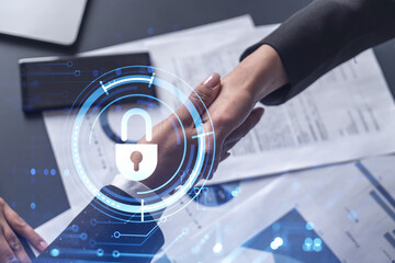 Handshake of two businesswomen who enters into the contract to protect cyber security of international company. Padlock Hologram icons over the table with documents.