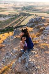 Mujer caucàsica sentada en la roca con rostro pensativo con la mirada perdida en la muela de alarilla durante el atardecer un día de verano 