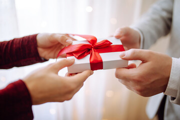 Valentine's day concept. A giftbox with red ribbon in hands. Loving couple give each other presents on 14 February. Romantic Boyfriend and girlfriend celebrating lover's day.