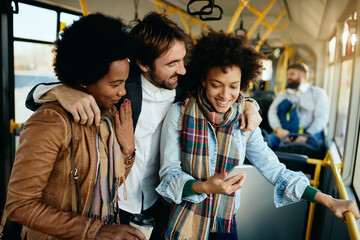 Happy friends having fun while using mobile phone in a public transport.