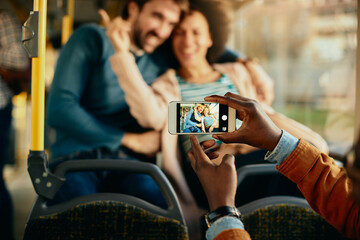 Close-up of a man photographing happy couple with cell phone in a bus.
