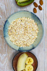 Ingredients for making porridge, oatmeal, nuts almond, banana, kiwi top view, healthy food and hearty breakfast with fruits