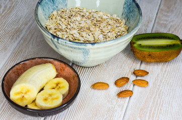 Ingredients for making porridge, oatmeal, nuts almond, banana, kiwi top view, healthy food and hearty breakfast with fruits