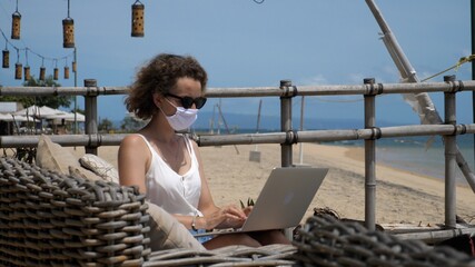 Remote working at the beach during corona virus. Female in a face mask in beach restaurant
