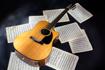 Fototapeta na wymiar set of sheet music scores and classical acoustic six-string yellow guitar with black pickguard on isolated black background