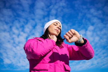 Sportswoman in winter training clothes measuring her pulse after running on snow.