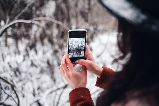 Traveler takes photo of snowy landscape in winter forest on mobile phone