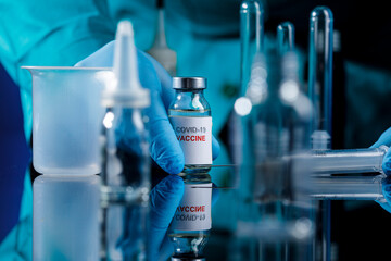 dettaglio delle mani di un Medico con protezioni e guanti in lattice che prende  il vaccino anti-covid con le dita da un tavolo di un laboratorio 