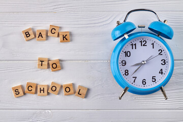 Blue alarm clock on white wood. Back to school concept.