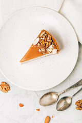 A piece of cheesecake with salted caramel and nuts on a plate.